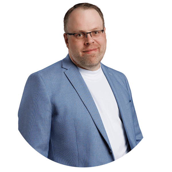 Florian-Gypser-Tonmeister Ein Mann mit Brille, hellblauem Blazer und weißem Hemd steht vor einem schlichten weißen Hintergrund und blickt mit einem leichten Lächeln in die Kamera.