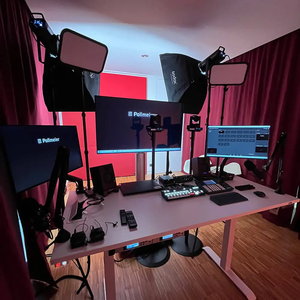 3Schritte_02 Ein professionelles Streaming-Setup mit drei Monitoren, zwei großen Softbox-Lichtern, verschiedenen Kameras, Audiogeräten und Bedienfeldern auf einem weißen Pult, alles vor roten Vorhängen und einem Holzboden.