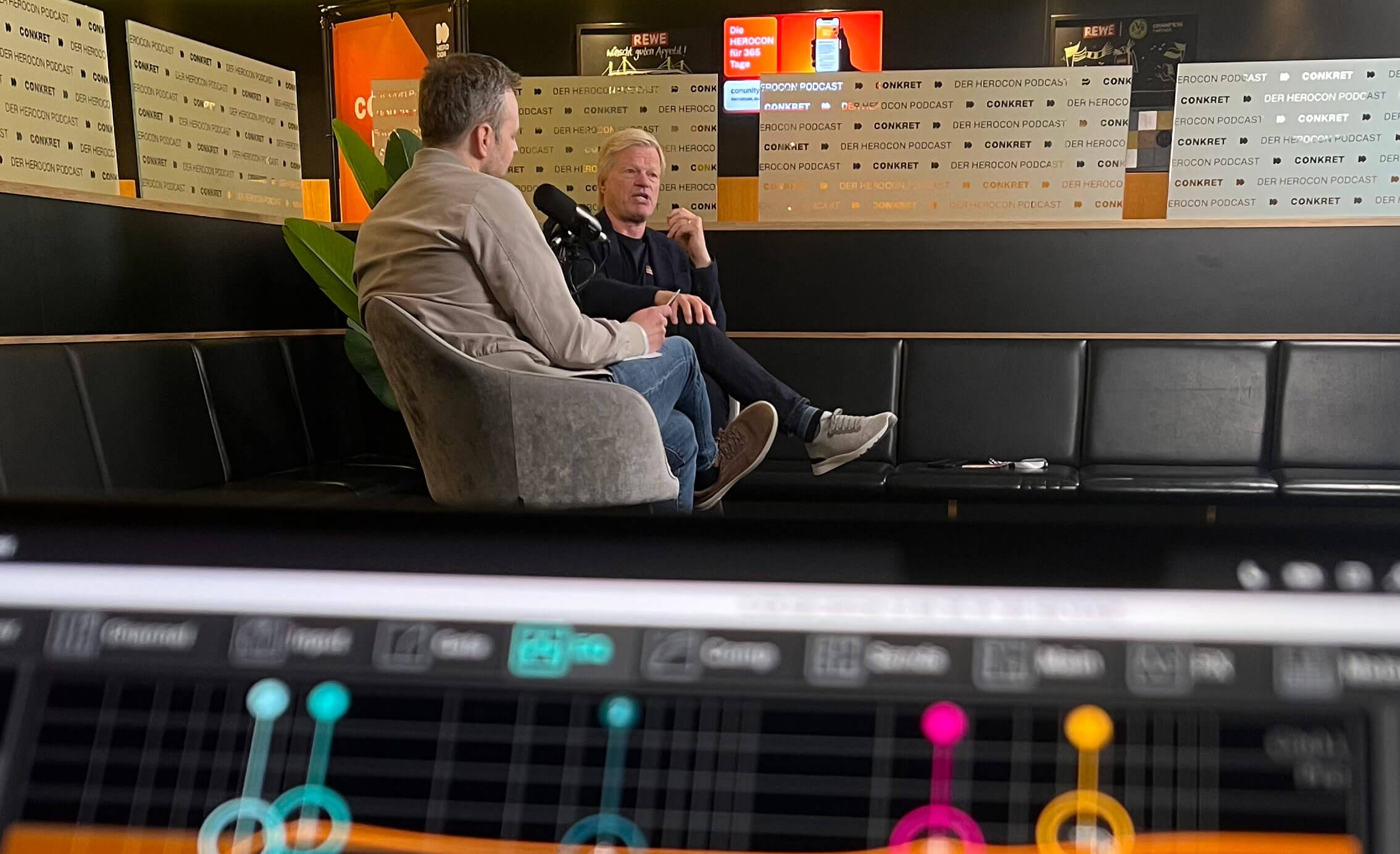 Zwei Männer sitzen auf einem schwarzen Sofa in einem modernen Studio und unterhalten sich vor Mikrofonen. Im Vordergrund ist ein unscharfes Mischpult zu sehen, im Hintergrund sind Banner des „CONNECT“-Podcasts zu erkennen.